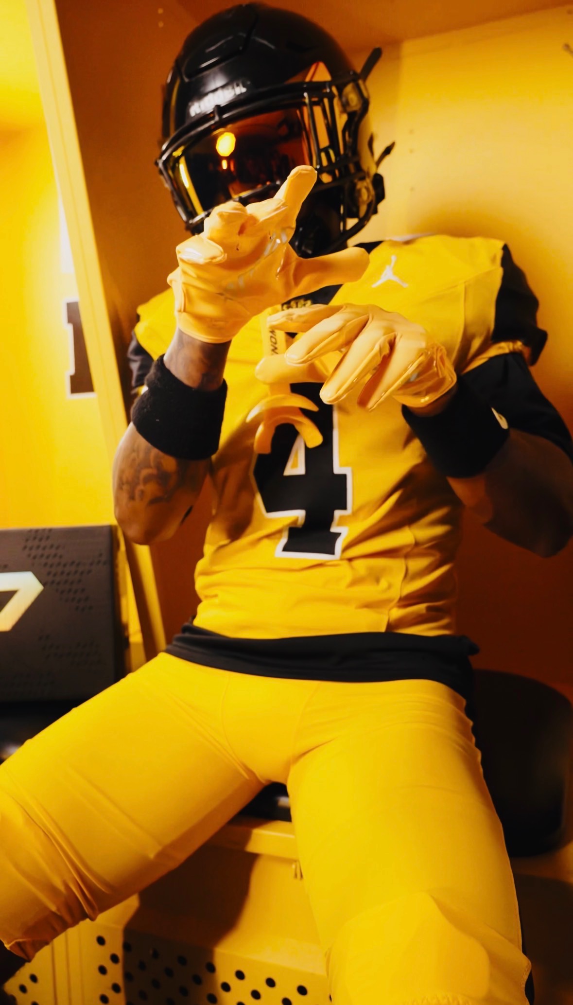 A football player in a yellow uniform and black helmet posing in a locker room